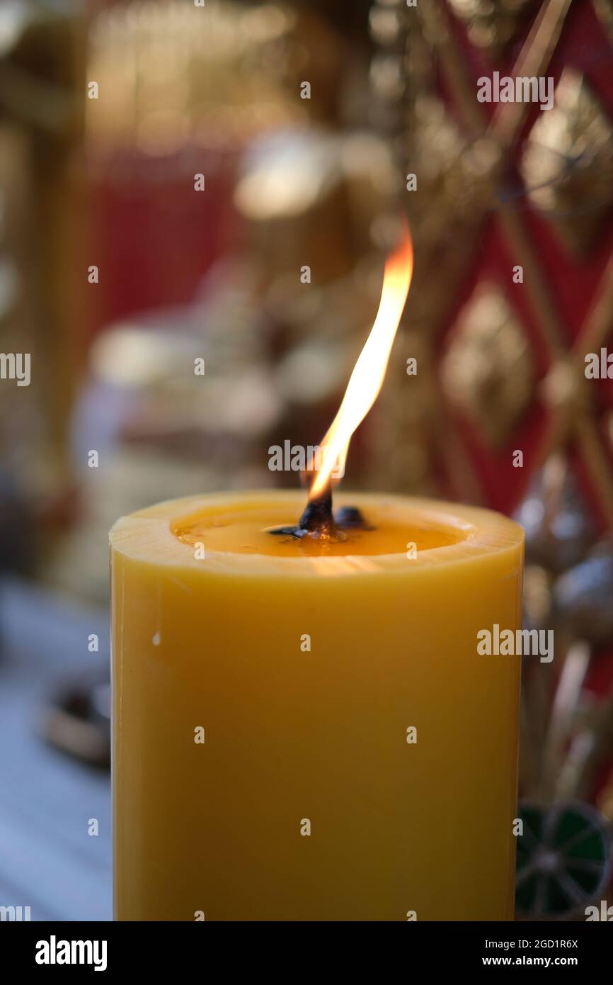 Una spessa candela illuminata contro uno sfondo di simboli religiosi in un tempio buddista nel nord della Thailandia Foto Stock