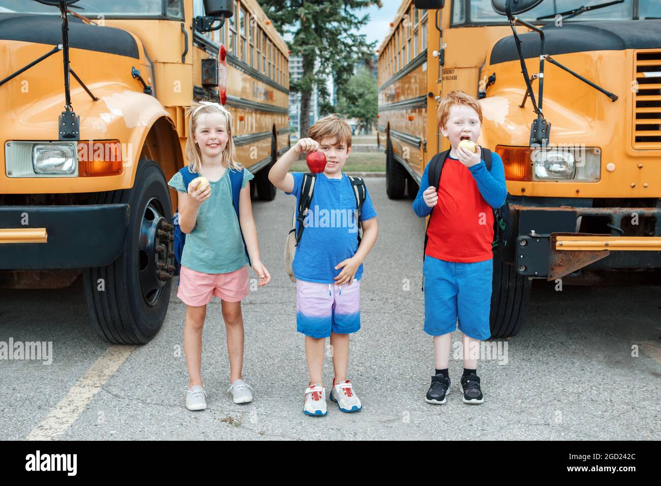 Bambini ragazzi e ragazze studenti amici mangiare mele snack sano da scuola bus giallo all'aperto. Istruzione e ritorno a scuola nel mese di settembre. Foto Stock