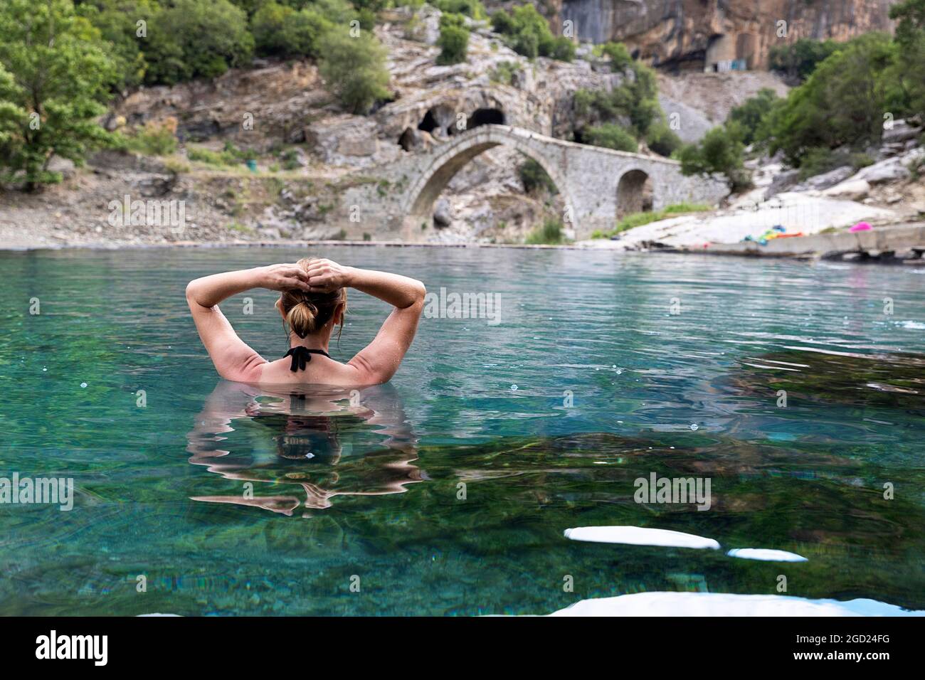 Donna godendo in bagni termali a Benje, ottomano ponte arco di pietra dietro, fiume Lengarica, Përmet, Parco Nazionale Hotova-Dangell, Albania Foto Stock