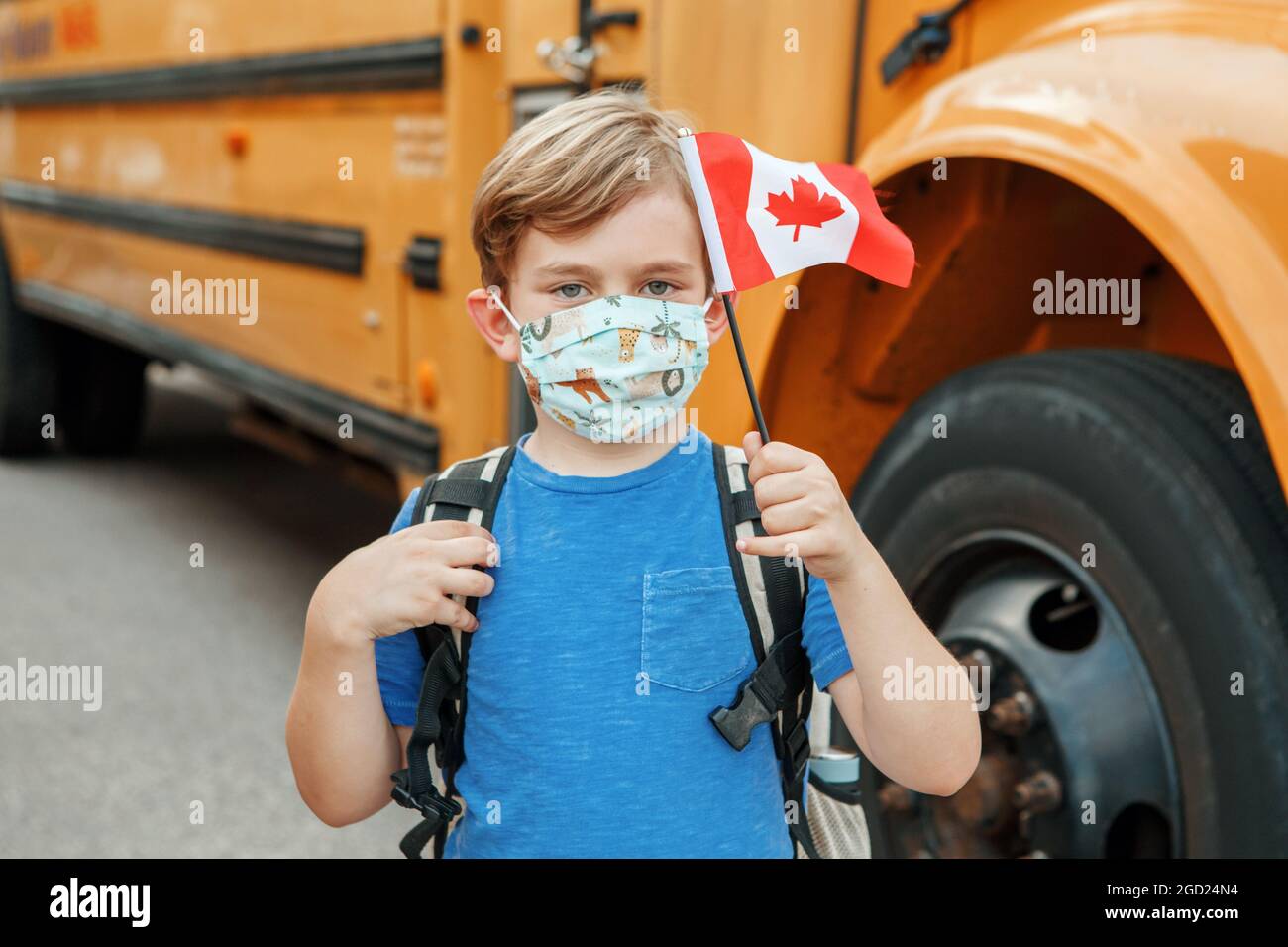 Orgoglioso bambino studente felice ragazzo con maschera facciale che tiene bandiera canadese. Istruzione e ritorno a scuola nel mese di settembre. Nuova normalità durante il coronavirus covid-19. Foto Stock