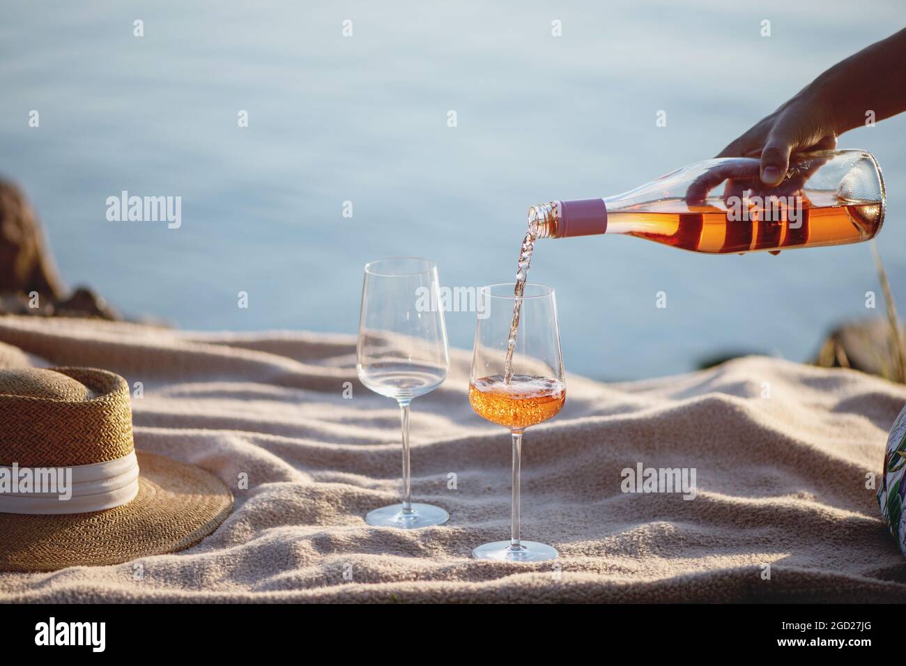 Donna mano versando vino rosato dalla bottiglia in bicchieri sulla spiaggia. Foto Stock