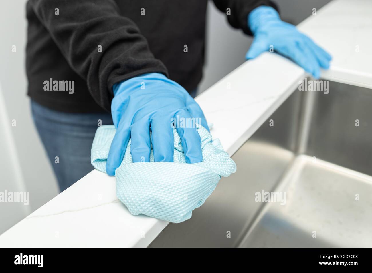 Mani in guanto protettivo pulizia di un moderno lavello con straccio di una cucina domestica minimalista Foto Stock