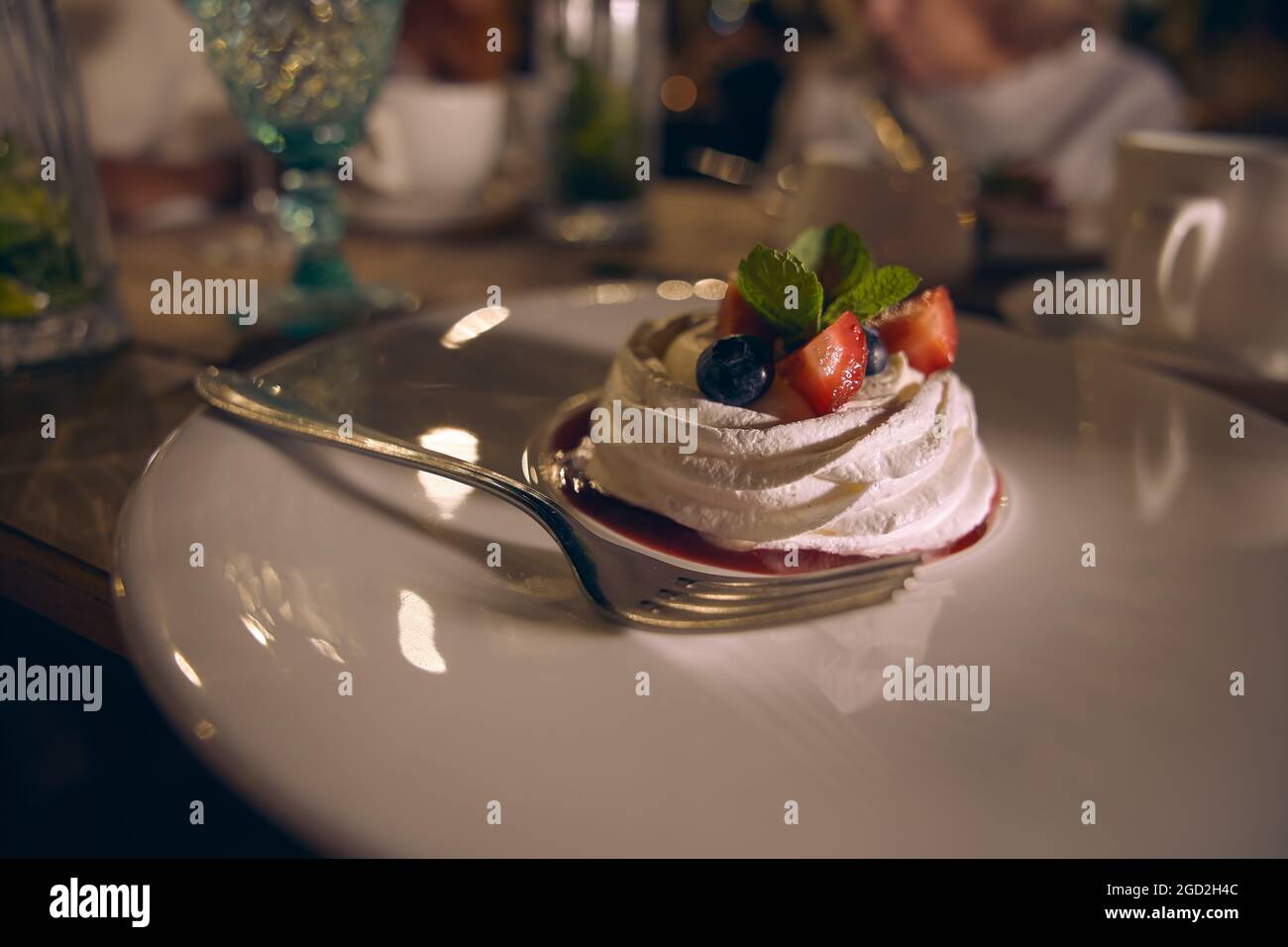 Meringa dolce torta Pavlova con fragole fresche, mirtilli e foglie di menta su un piatto di ceramica bianca. Foto Stock