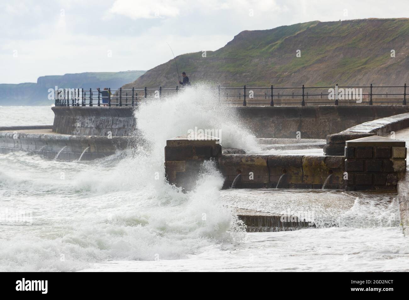 Uomo pesca con onde che si infrangono contro le difese marine nello Scarborough Yorkshire Foto Stock