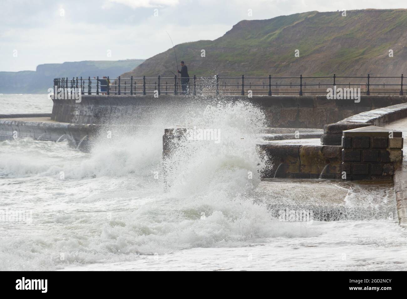 Uomo pesca con onde che si infrangono contro le difese marine nello Scarborough Yorkshire Foto Stock