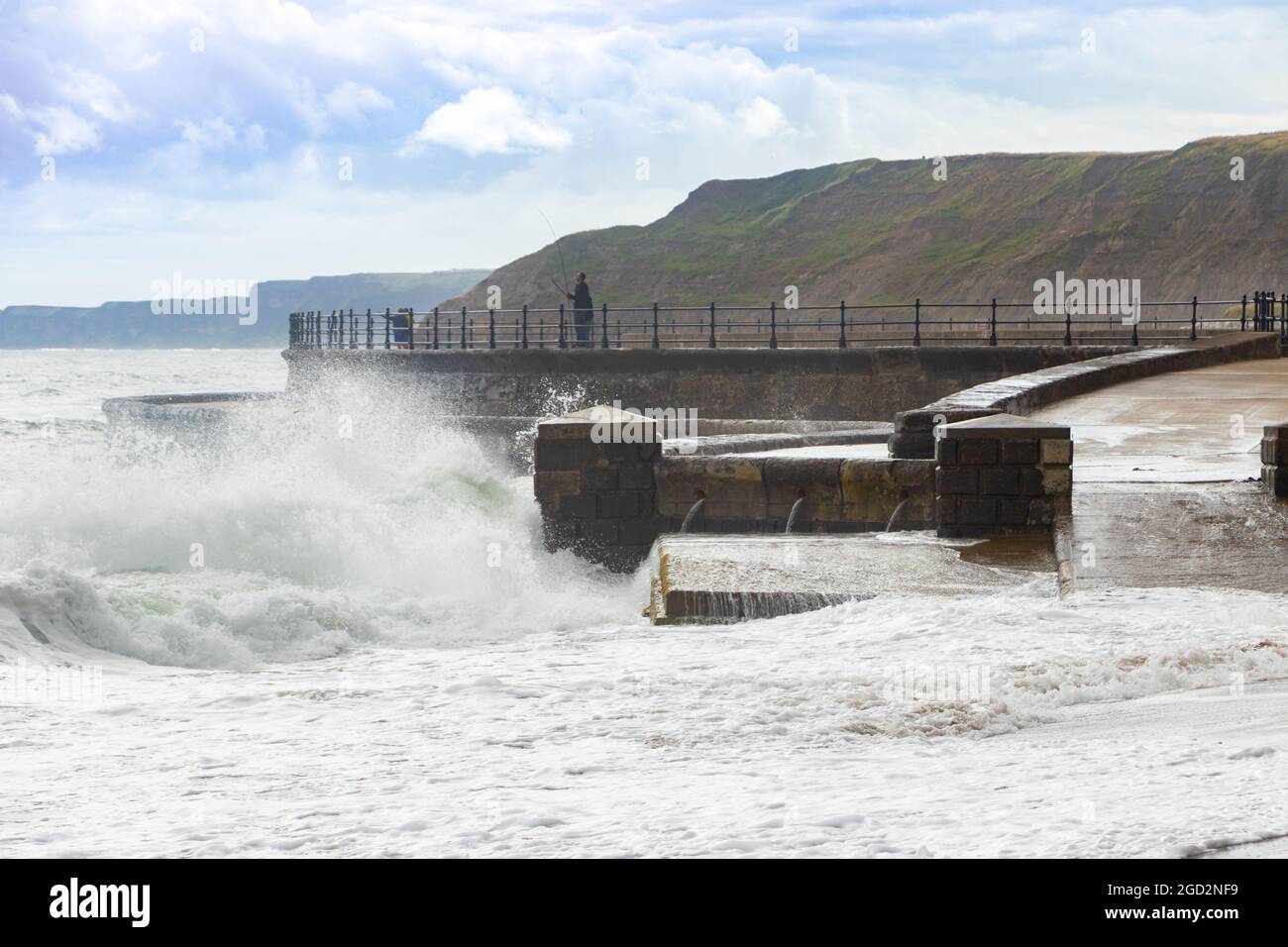 Uomo pesca con onde che si infrangono contro le difese marine nello Scarborough Yorkshire Foto Stock