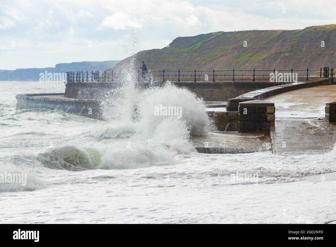 Uomo pesca con onde che si infrangono contro le difese marine nello Scarborough Yorkshire Foto Stock