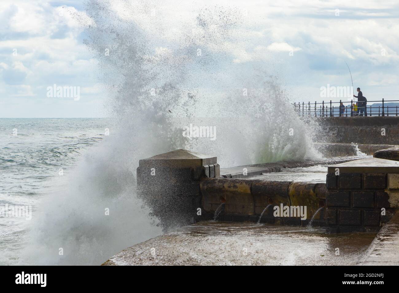 Uomo pesca con onde che si infrangono contro le difese marine nello Scarborough Yorkshire Foto Stock