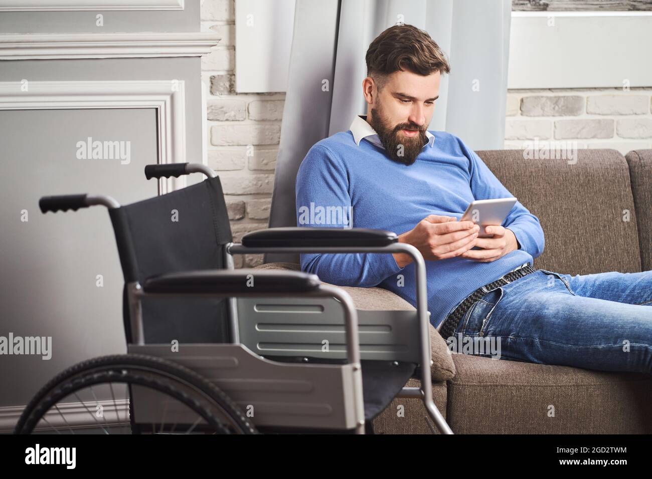 Uomo con disabilità che riposa su un divano e utilizza un computer tablet Foto Stock