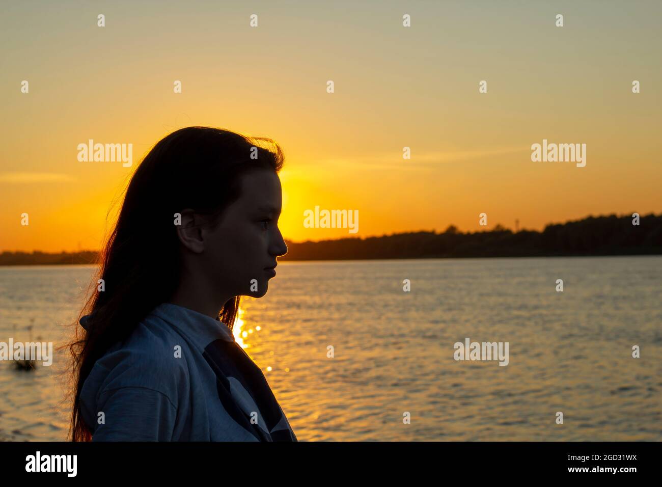 Silhouette della giovane ragazza sullo sfondo del tramonto sulla costa del fiume. Foto Stock