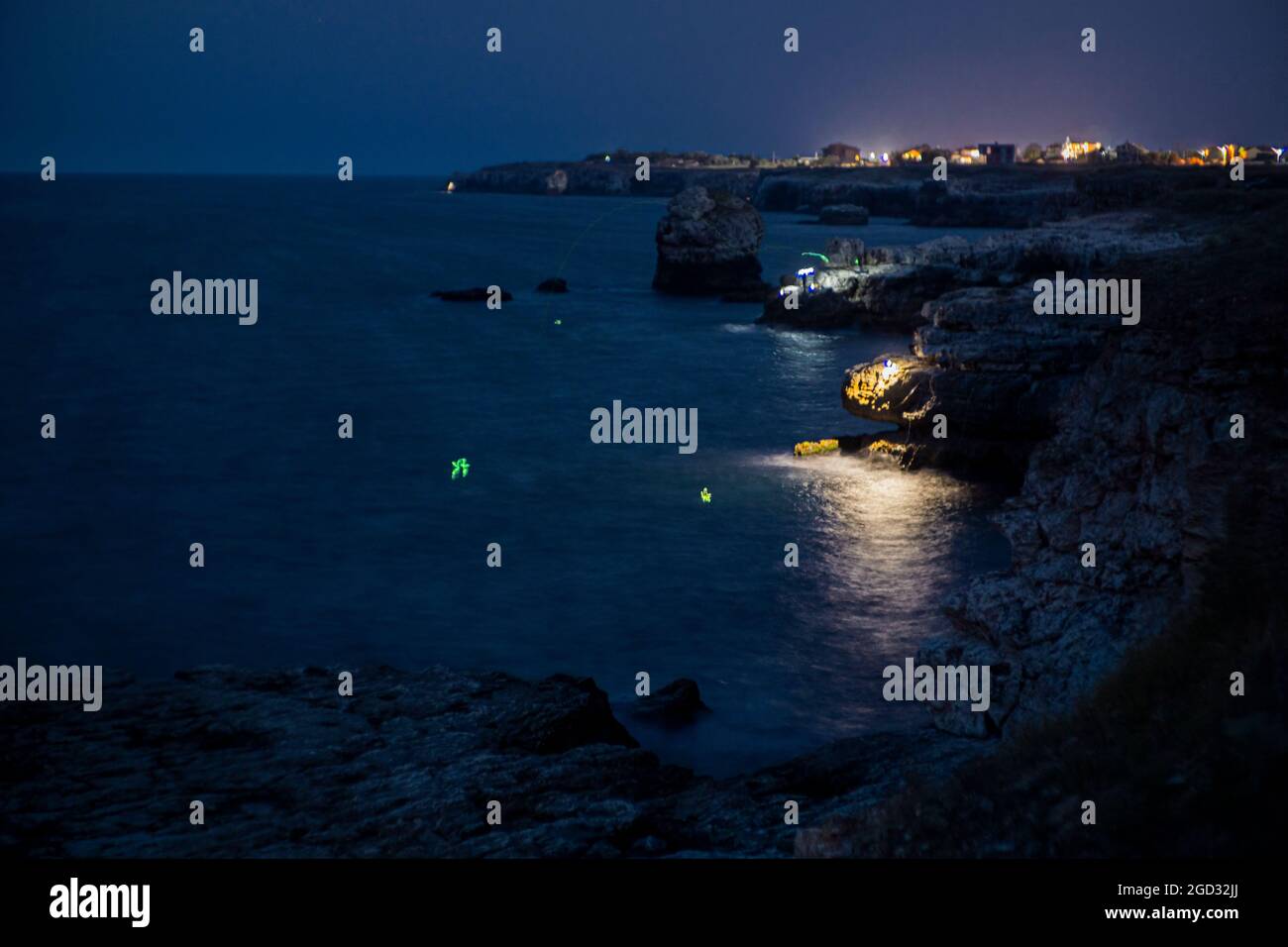 Pescatori durante la notte estrema pesca nella roccia illuminando il mare per attirare i pesci Foto Stock