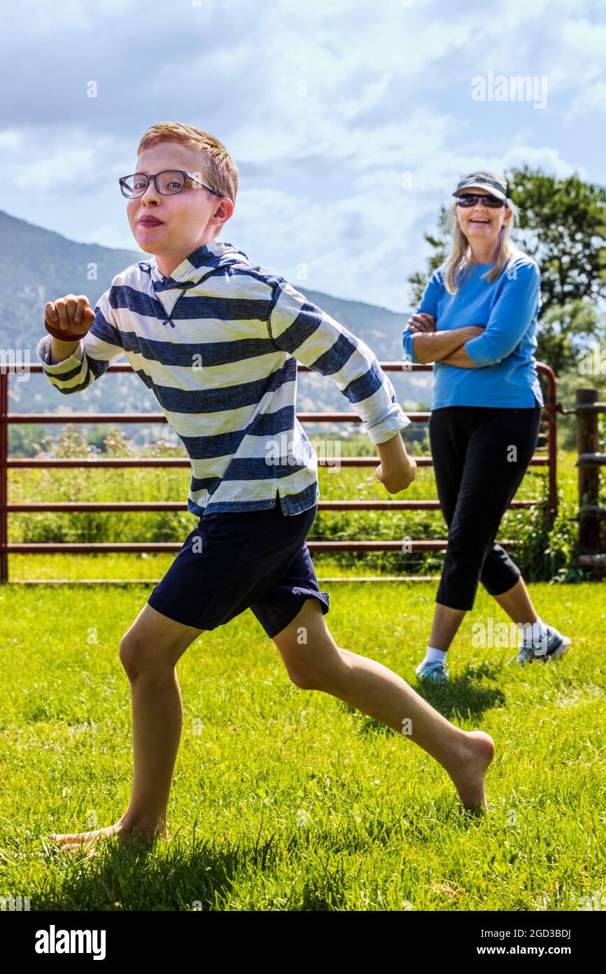 Donna ridente che guarda il ragazzo giovane che gioca e corre nel cortile erboso Foto Stock