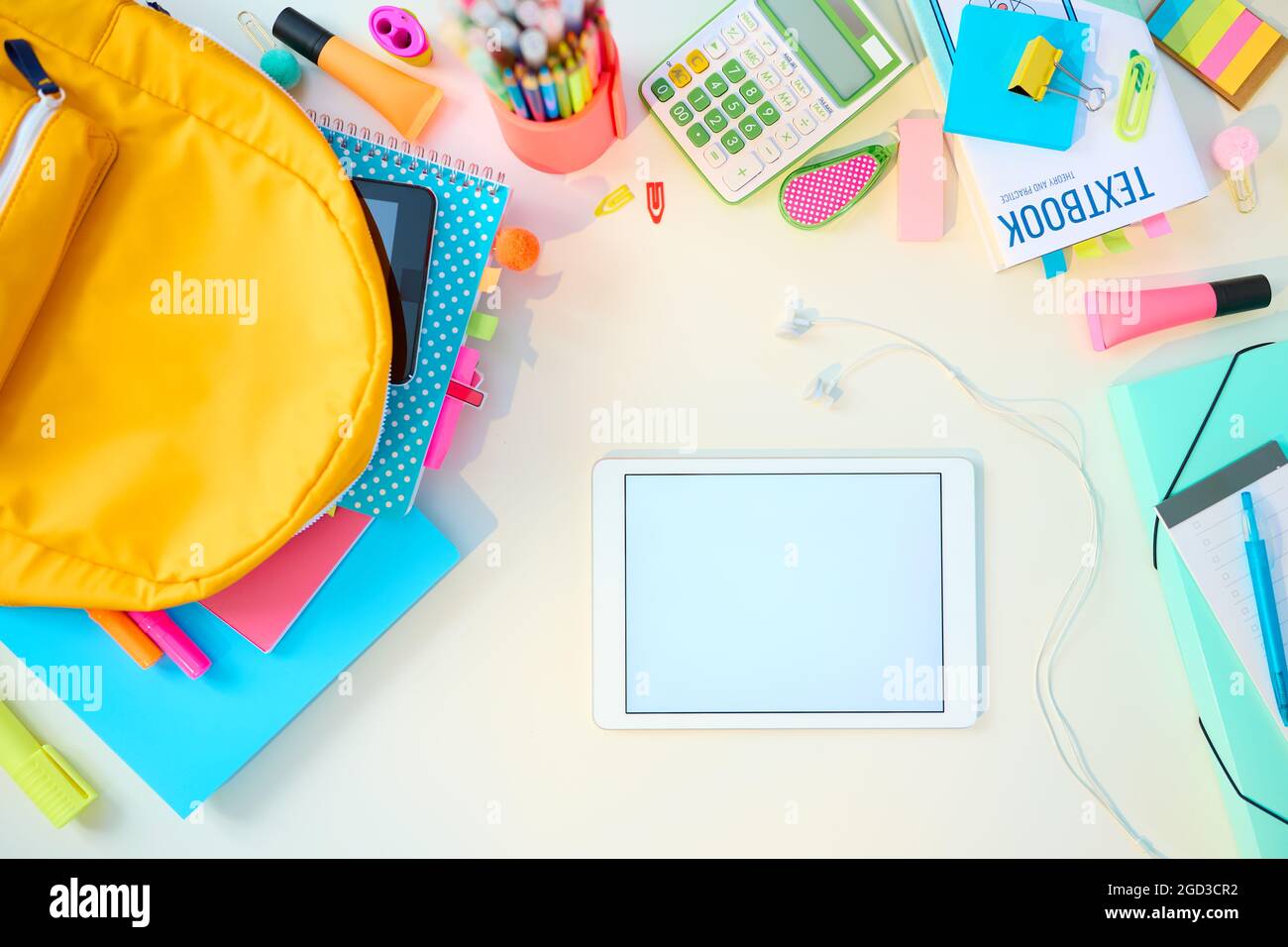 Ritorno a scuola. Vista superiore del tavolo bianco con libri da lavoro, cancelleria, libro di testo, tablet pc, zaino e cuffie nella stanza dei bambini della scuola in una giornata di sole. Foto Stock