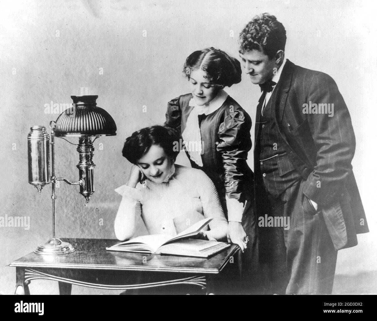 Giovani donne e giovani che leggono alla luce di una lampada brevettata tra il 1909 e il 1932 circa Foto Stock