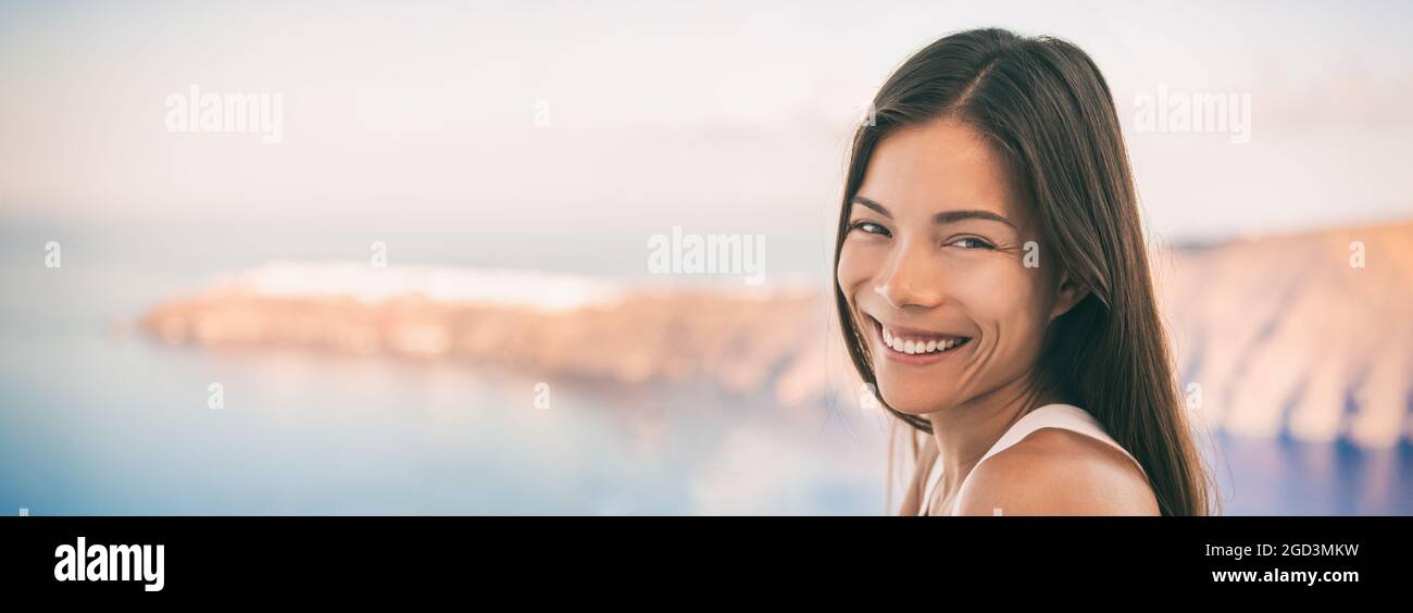 Donna asiatica giovane bella ragazza sorridente a macchina fotografica con vista panoramica di Oia grecia isola destinazione di viaggio. Vacanza crociera di lusso balcone esterno Foto Stock