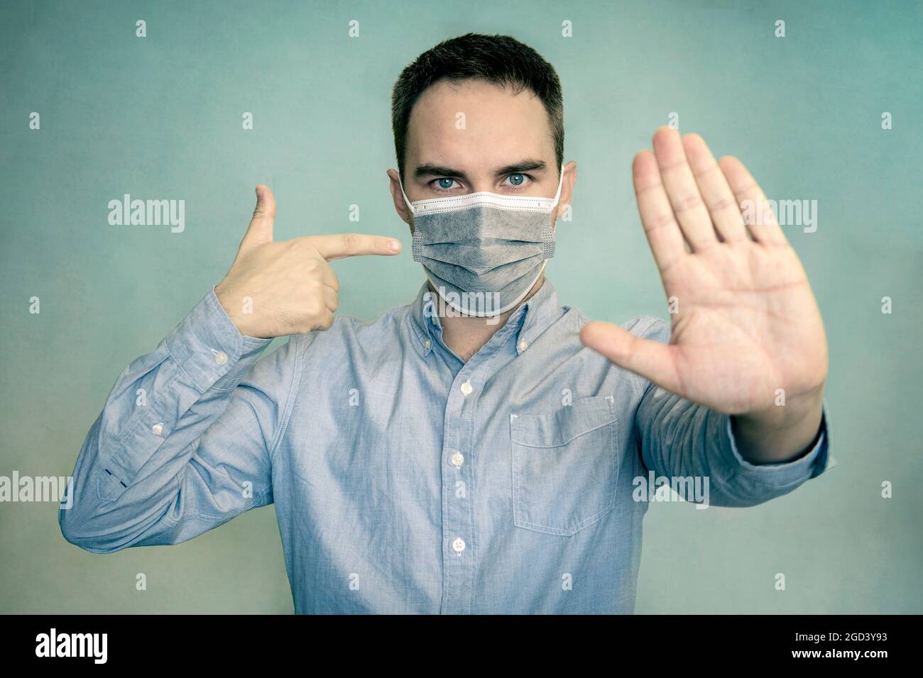 Ritratto di uomo serio mostra stop segno gesto avverte persone rimanere a casa indossare medico su sfondo di colore luminoso. Uso obbligatorio di una maschera in un pub Foto Stock