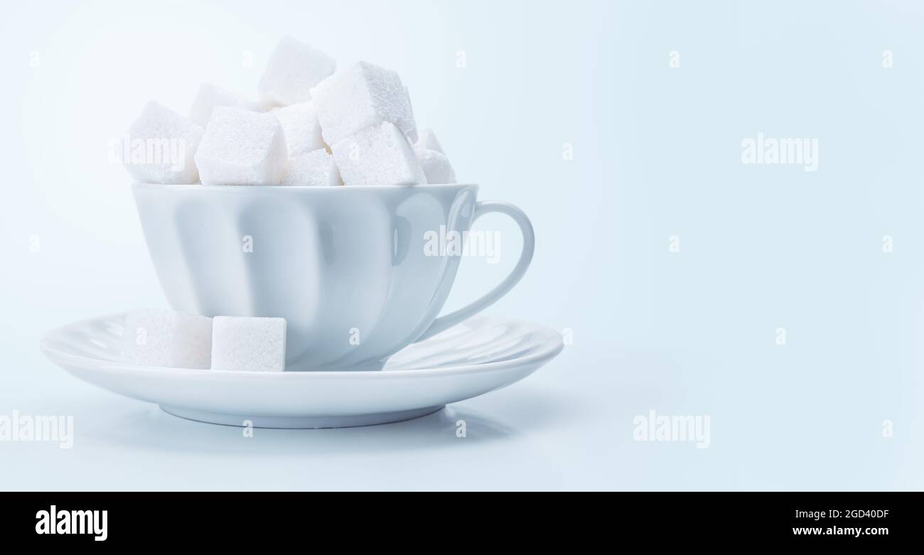 Tazza da tè piena di cubetti di zucchero bianco. Concetto di dipendenza alimentare malsana Foto Stock