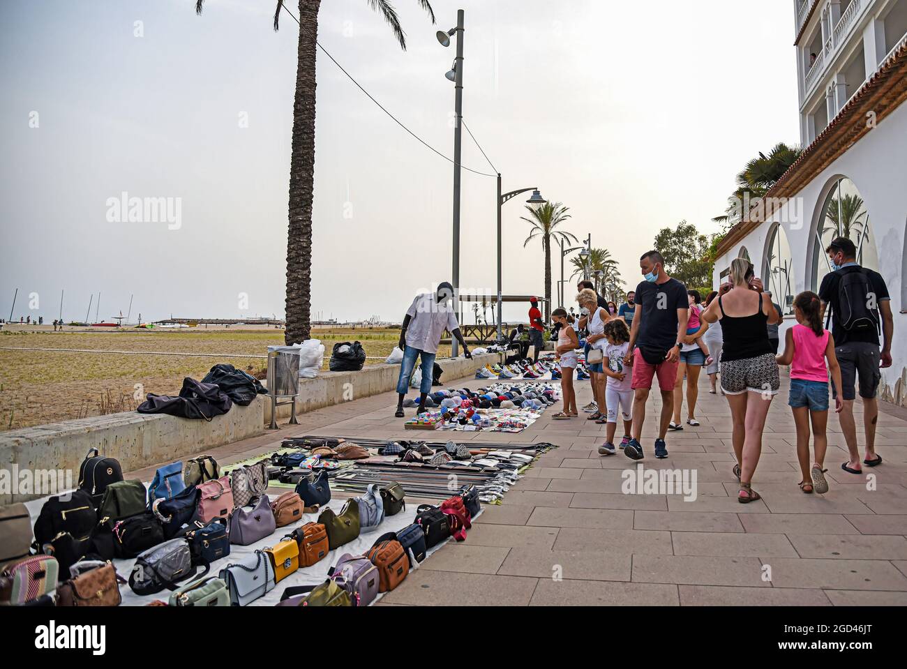 Vendrell, Spagna. 05 agosto 2021. Un venditore di strada mostra i suoi prodotti ad alcune persone su Paseo Maritimo Street a Vendrell. I venditori illegali di strada conosciuti come 'Mantero' o 'Top Manta', principalmente di nazionalità senegalese, che vendono prodotti contraffatti da borse, sneakers, occhiali, marchi come Nike, Adidas, Louis Vuitton, Ray-Ban tra gli altri approfittano dell'arrivo dei turisti a Vendrell per vendere i loro prodotti in tempi della pandemia. Credit: SOPA Images Limited/Alamy Live News Foto Stock