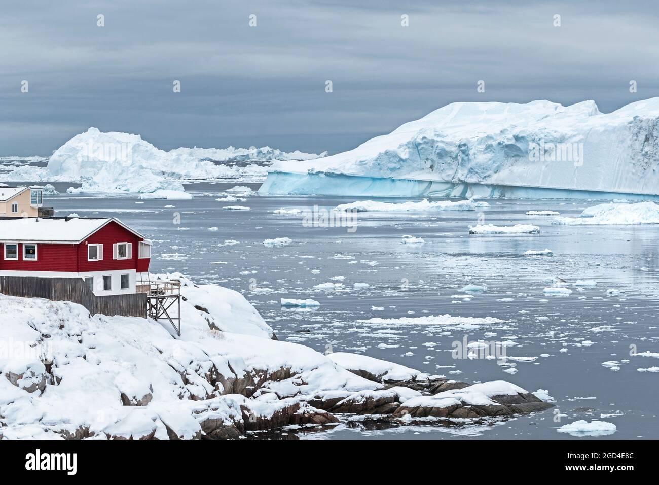 Casa cittadina rossa si erge sulla riva in inverno. Ilulissat, Disko Bay, Groenlandia Foto Stock