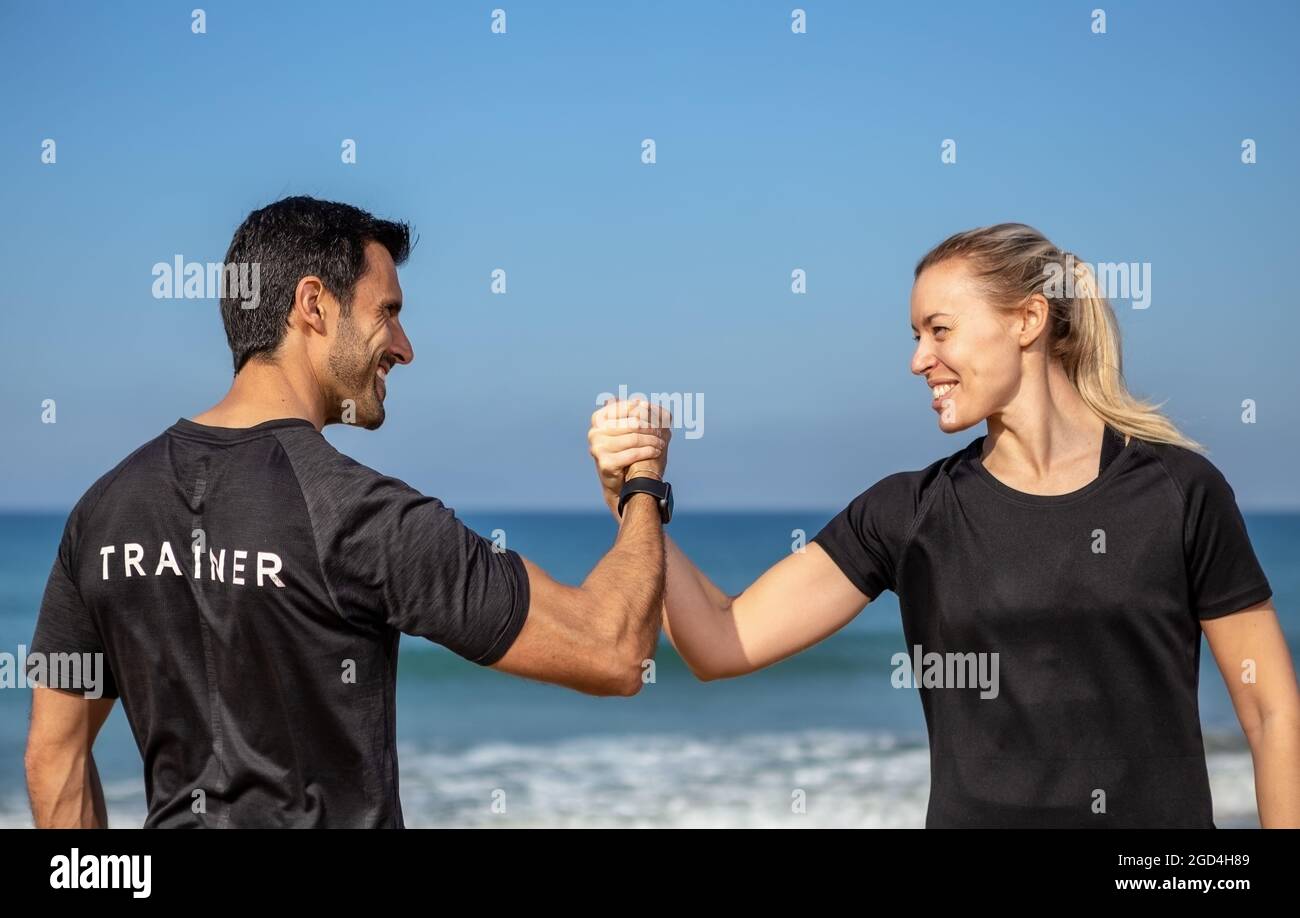 Un allenatore di fitness e un cliente, una donna europea, scuotono le mani. Sullo sfondo del mare in estate. Foto Stock