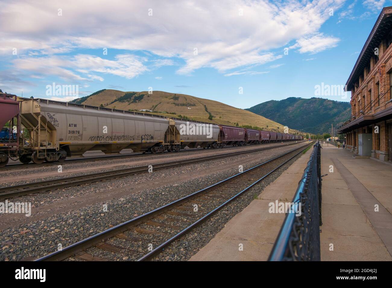 Treno auto allineate di fronte alle colline vicino alla vecchia stazione ferroviaria di mattoni marroni, deposito per la ferrovia del Pacifico settentrionale. A Missoula, Montana. Foto Stock