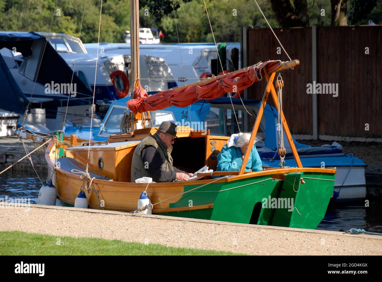 Coppie anziane che si rilassano all'aria aperta su uno yacht ormeggiato sul Norfolk Broads, Inghilterra, in una fresca giornata autunnale con entrambi i cappotti per mantenere caldo Foto Stock