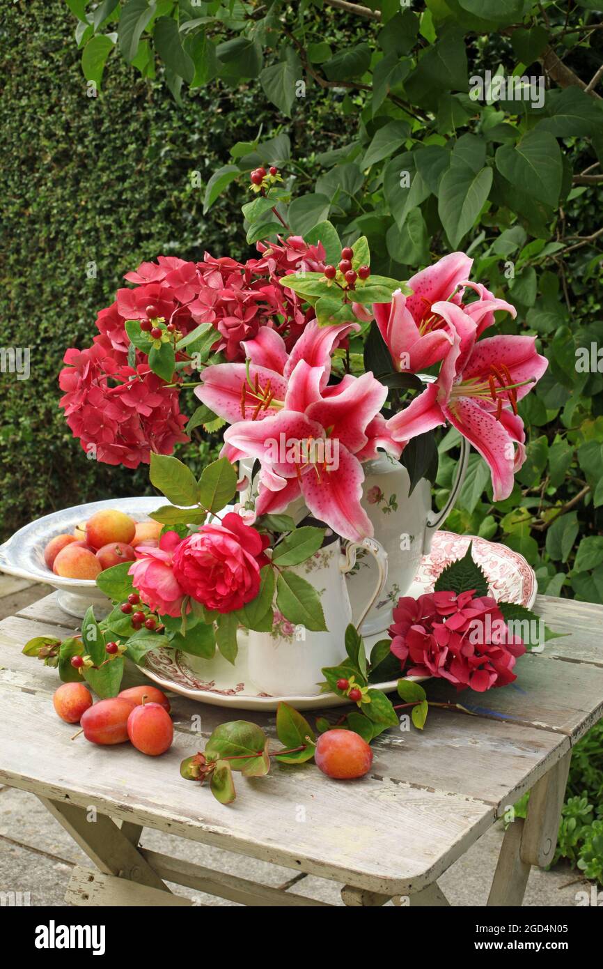 Botanica, iperico, rose, lilium e idrangea in brocche su un tavolo all'aperto con prugne, DIRITTI-AGGIUNTIVI-CLEARANCE-INFO-NON-DISPONIBILE Foto Stock