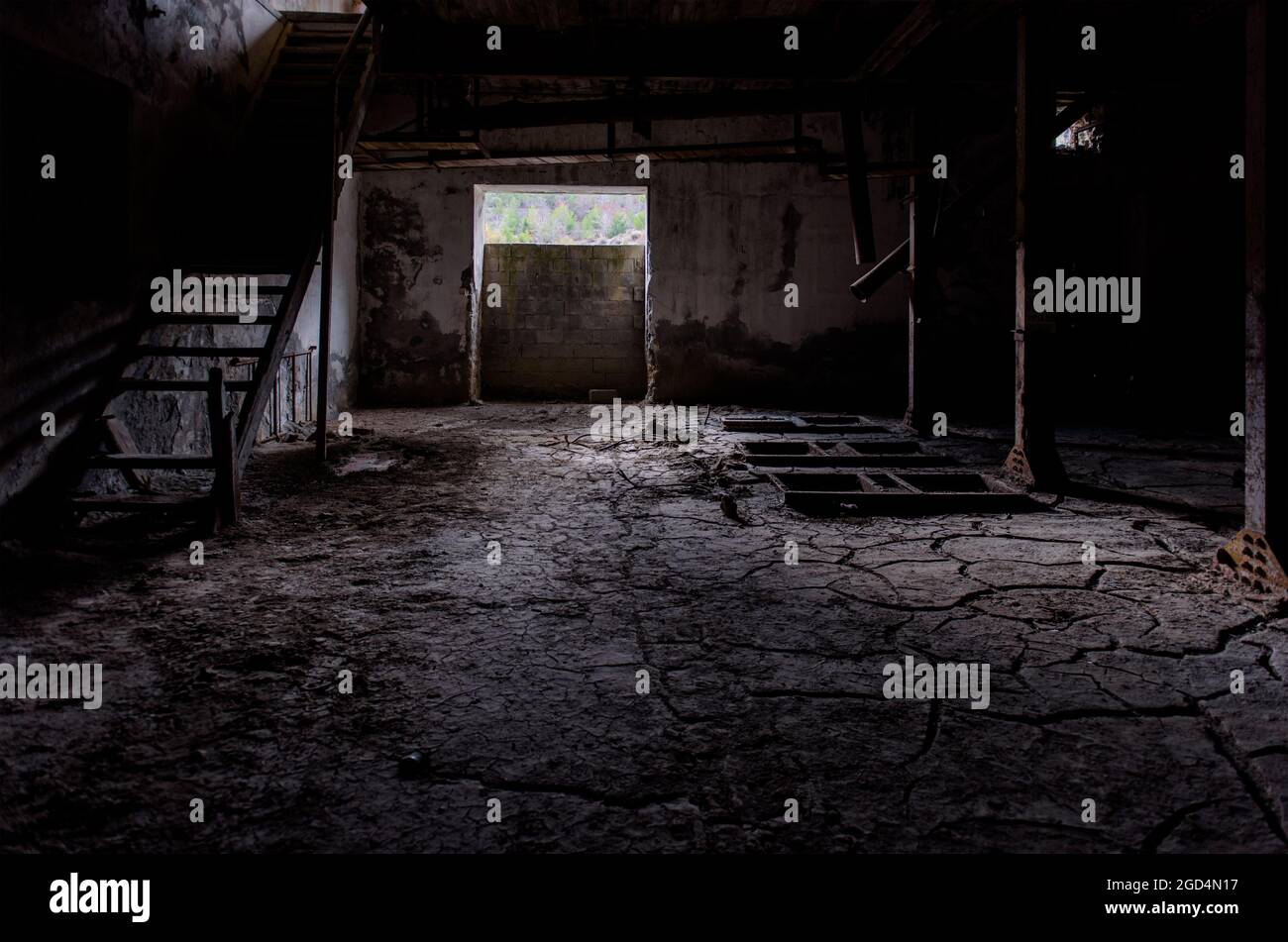 Vecchio sfondo interno di fabbrica. Camera oscura con sporcizia incrinata sul pavimento, scale di legno rotte e resti arrugginiti di macchinari Foto Stock