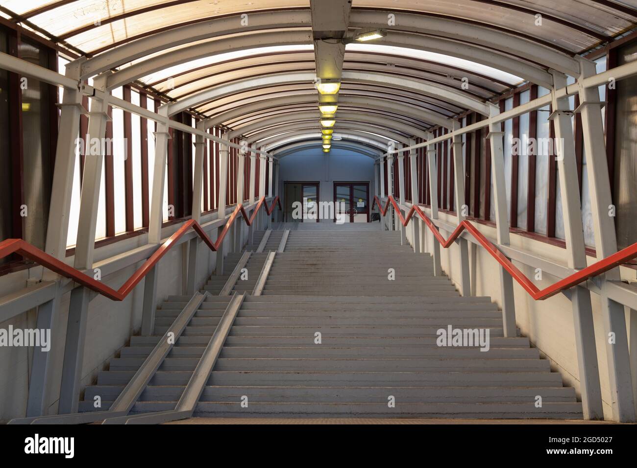 Scale in un passaggio coperto con corrimano e una rampa per sedie a rotelle che porta alle porte Foto Stock