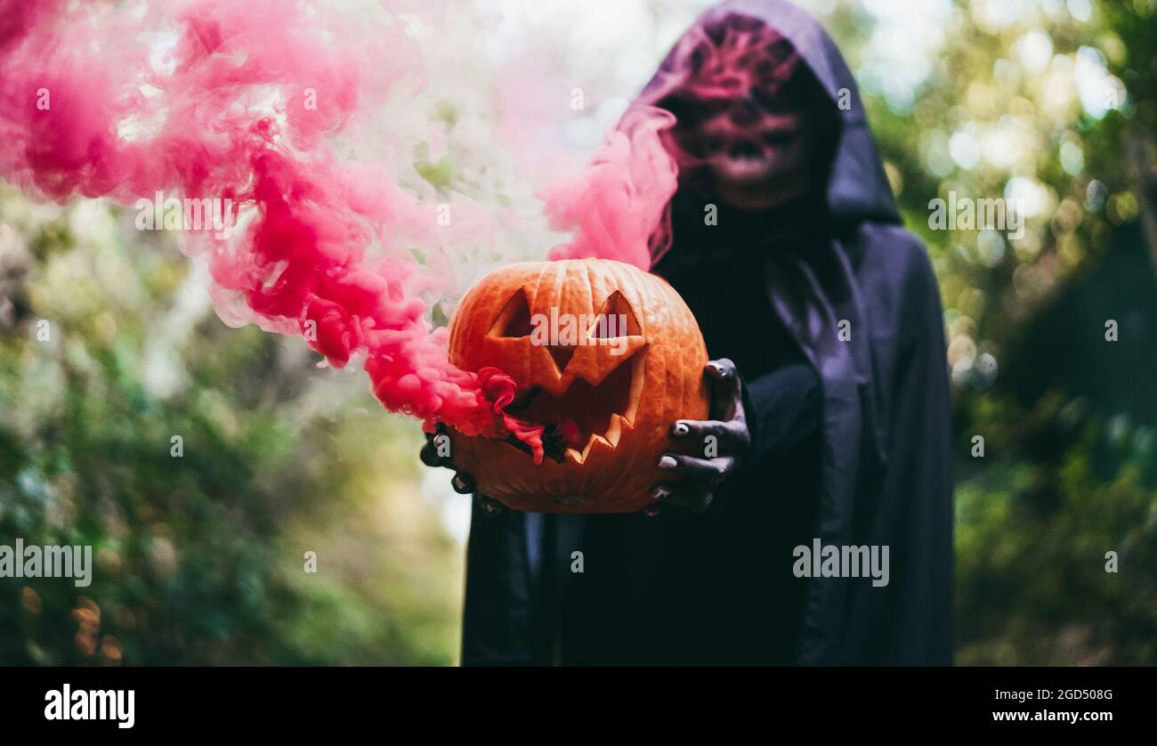 Ragazza con costume di Halloween e compongono tenendo la zucca con una bomba di fumo all'interno - fuoco sulle mani che tengono la zucca Foto Stock