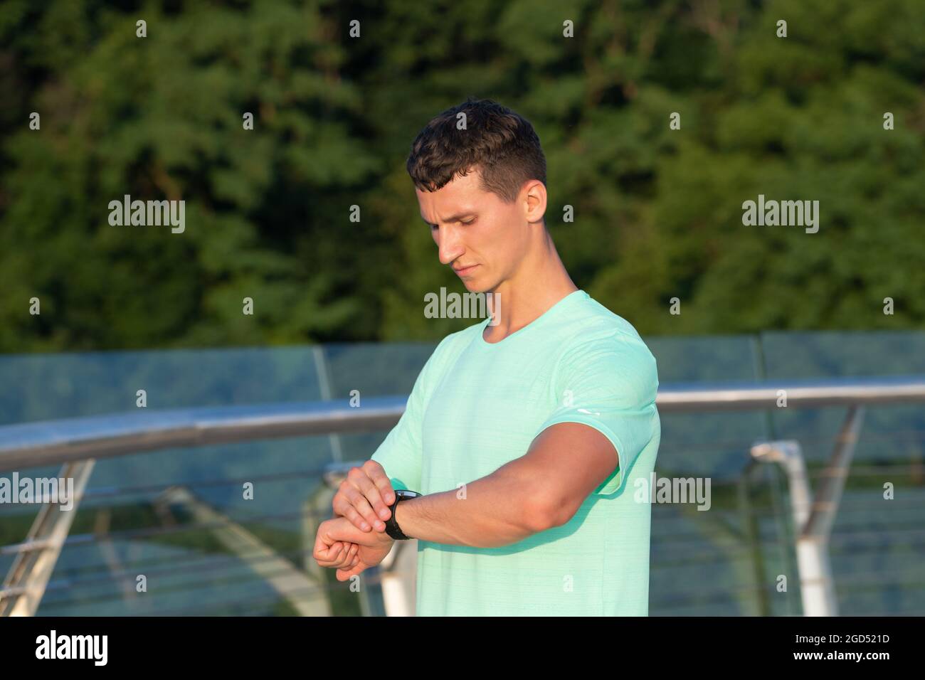 L'uomo atletico controlla il tempo sull'orologio da polso durante l'allenamento all'aperto, i tempi sportivi Foto Stock