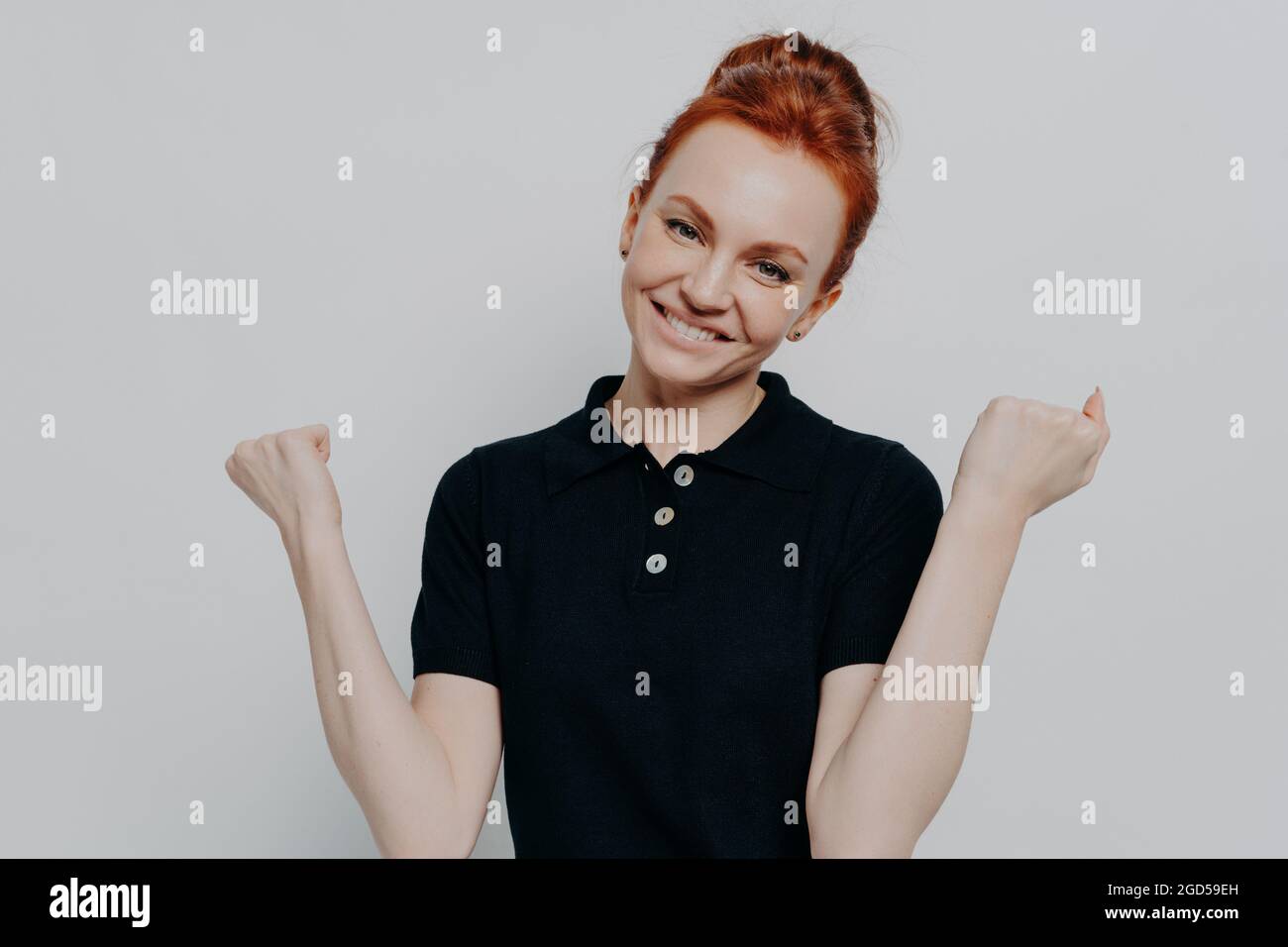 Studio di felice caucasica rosso donna clenching pugni e sorridente felicemente Foto Stock