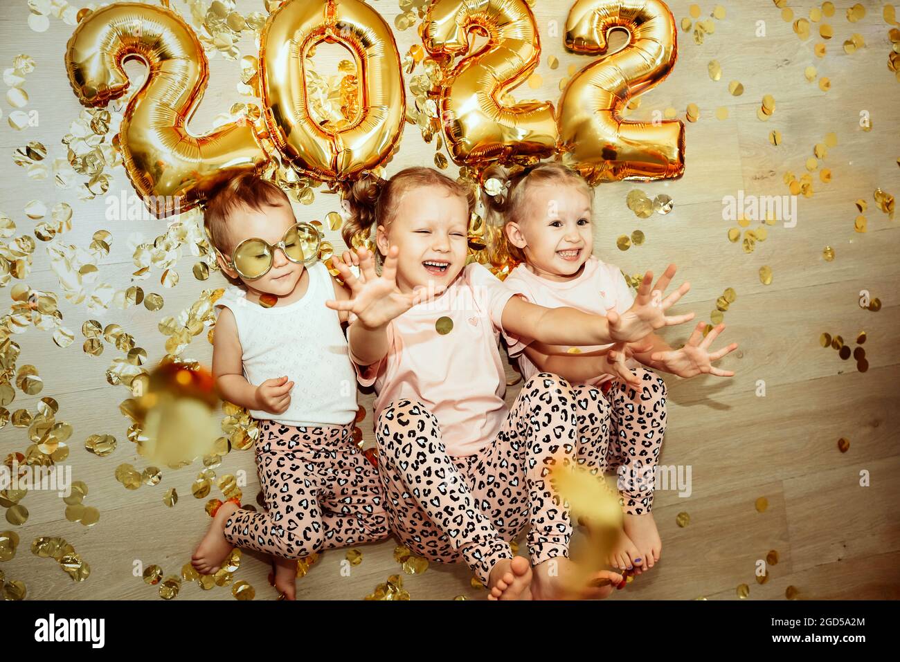 I bambini, 3 sorelle, celebrano il nuovo anno 2022 a casa, si sciogliano e ridono in confetti. Festeggiamo i nuovi anni e il Natale a casa durante il Covid- Foto Stock