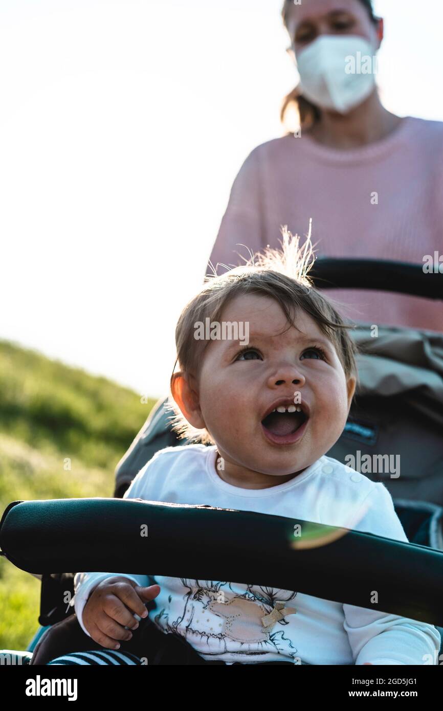 Ridendo bambina godendo una passeggiata in un parco seduto nel passeggino moderno durante l'epidemia di coronavirus - bambino dolce in buggy mostrando i primi denti dentro Foto Stock
