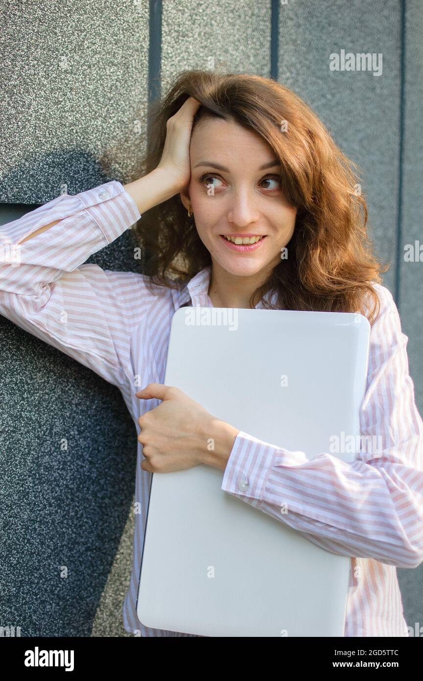 Ritratto femminile di giovane donna con notebook argento, donna d'affari sta posando con tablet digitale all'esterno su sfondo scuro della parete mentre aspetta un Foto Stock