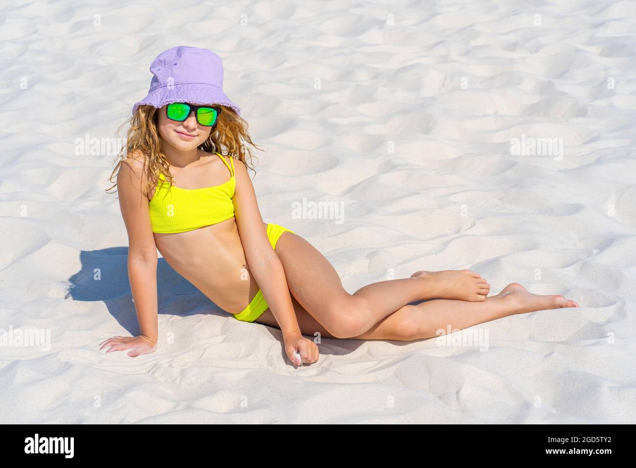 Ritratto di una giovane bella modella ragazza con cappello e occhiali da  sole in posa sulla spiaggia. Indossa un costume da bagno bikini giallo  brillante. Giorno d'estate, sabbia bianca. Foto di alta
