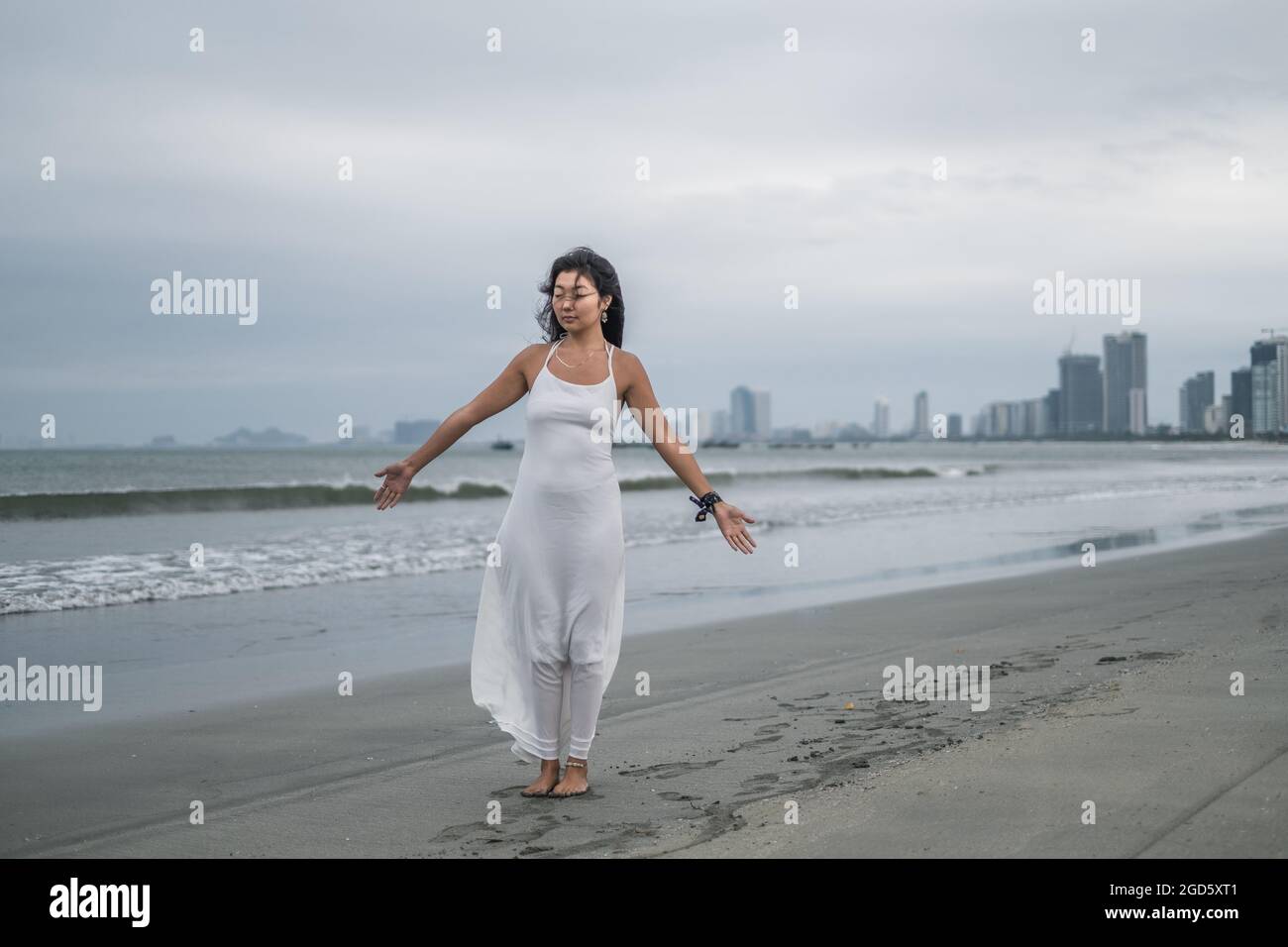Affascinante giovane donna asiatica in abito bianco si alza con le mani a lato sulla spiaggia. Foto romantica e tranquilla. Foto di alta qualità Foto Stock