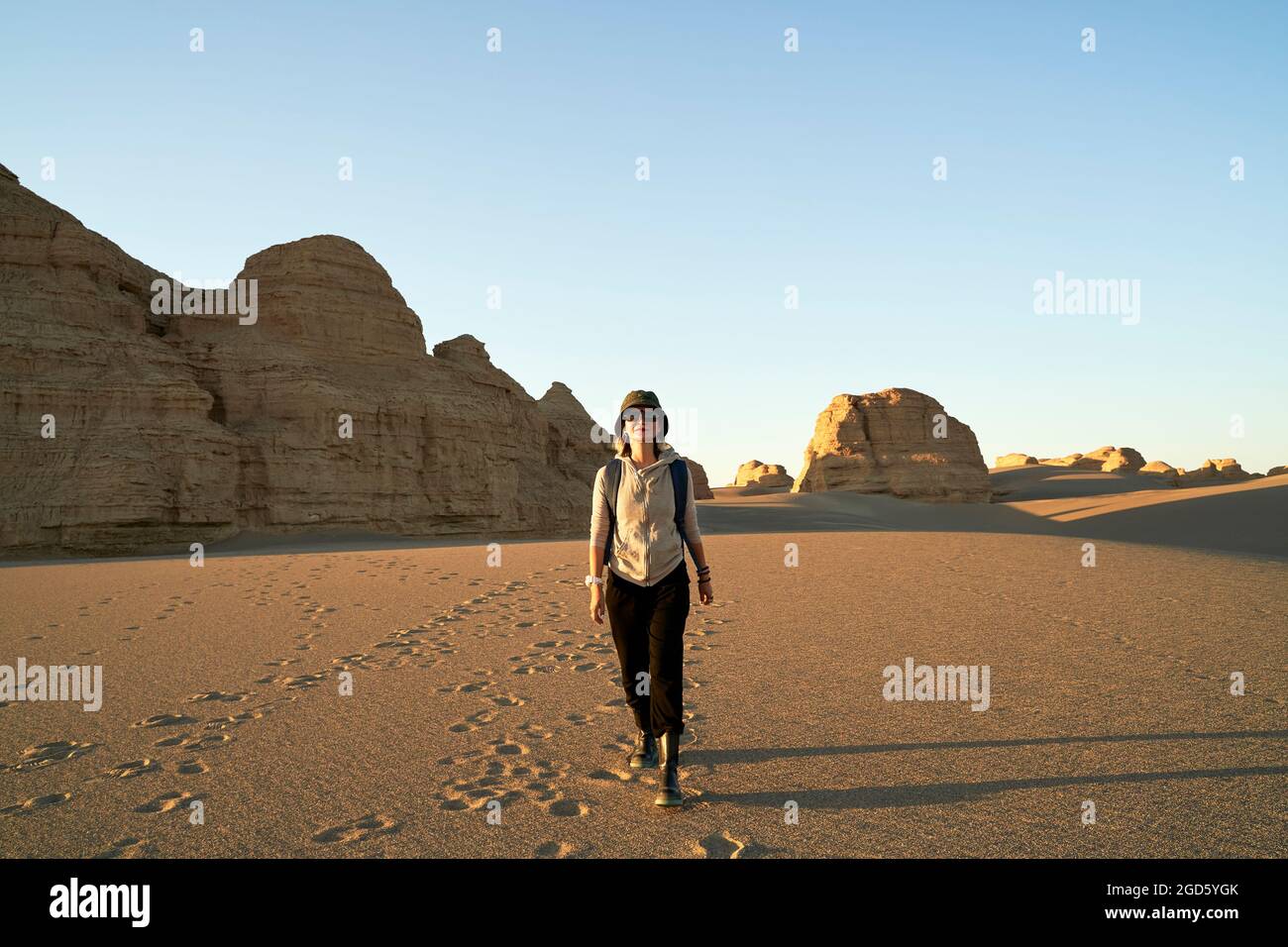 donna asiatica viaggiatore zaino in spalla a piedi nel deserto al tramonto con yardang landform in background Foto Stock
