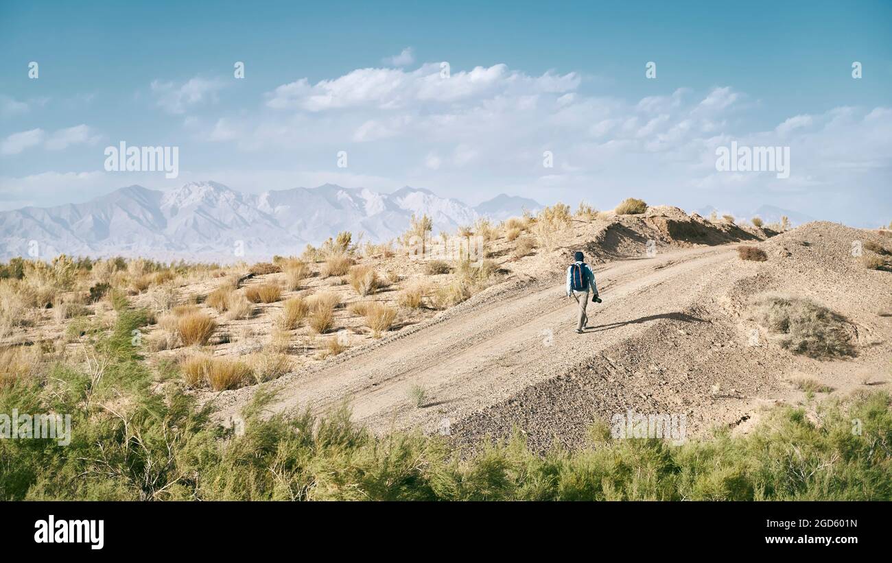 vista posteriore di un uomo asiatico zaino in spalla fotografo camminare su una strada sterrata attraverso il deserto di gobi Foto Stock