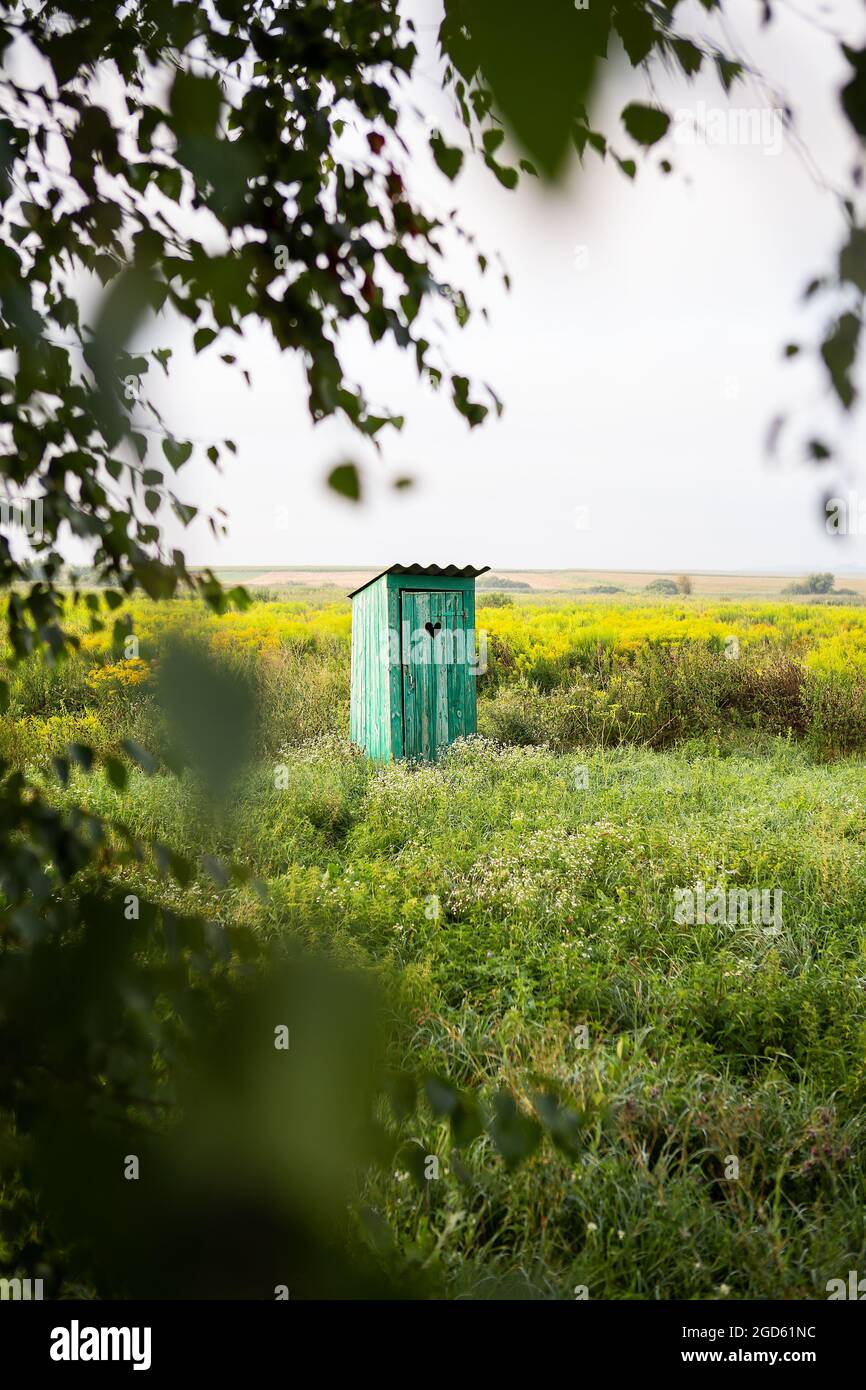 wc d'epoca nel mezzo di un campo di fiori. un wc verde rustico all'aperto con un cuore tagliato fuori sulla porta Foto Stock