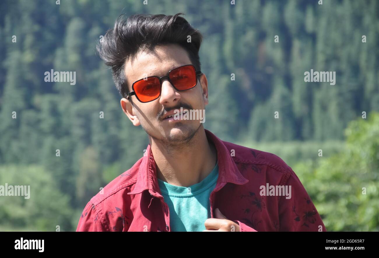 Primo piano di un giovane ragazzo dell'India del Nord in posa all'aperto con una camicia rossa e occhiali da sole rossi da guardare con la macchina fotografica Foto Stock