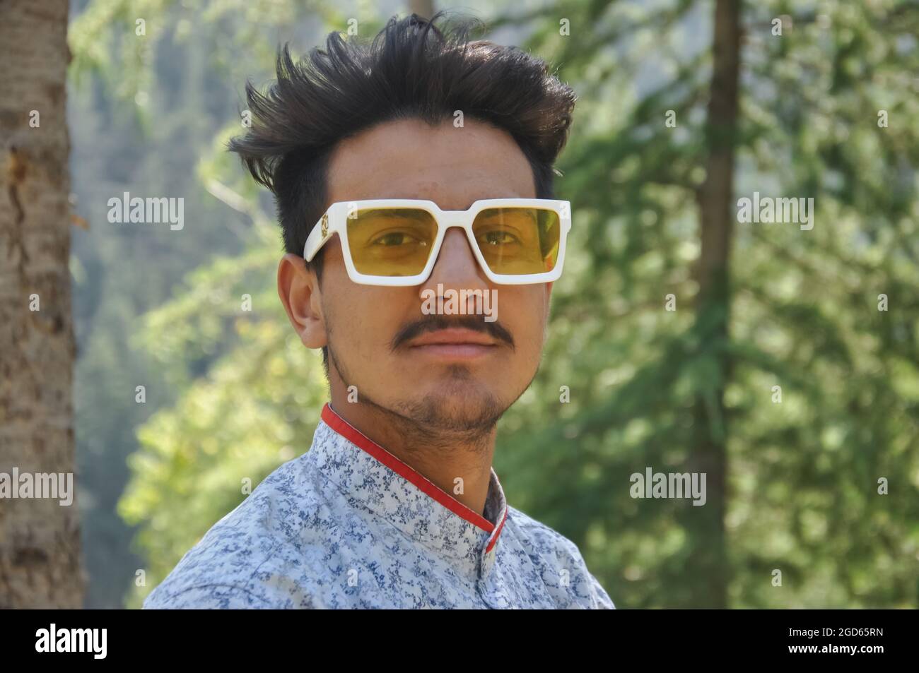 Primo piano di un giovane ragazzo di buon aspetto in piedi all'aperto nella natura e indossare occhiali da sole con guardare la macchina fotografica Foto Stock