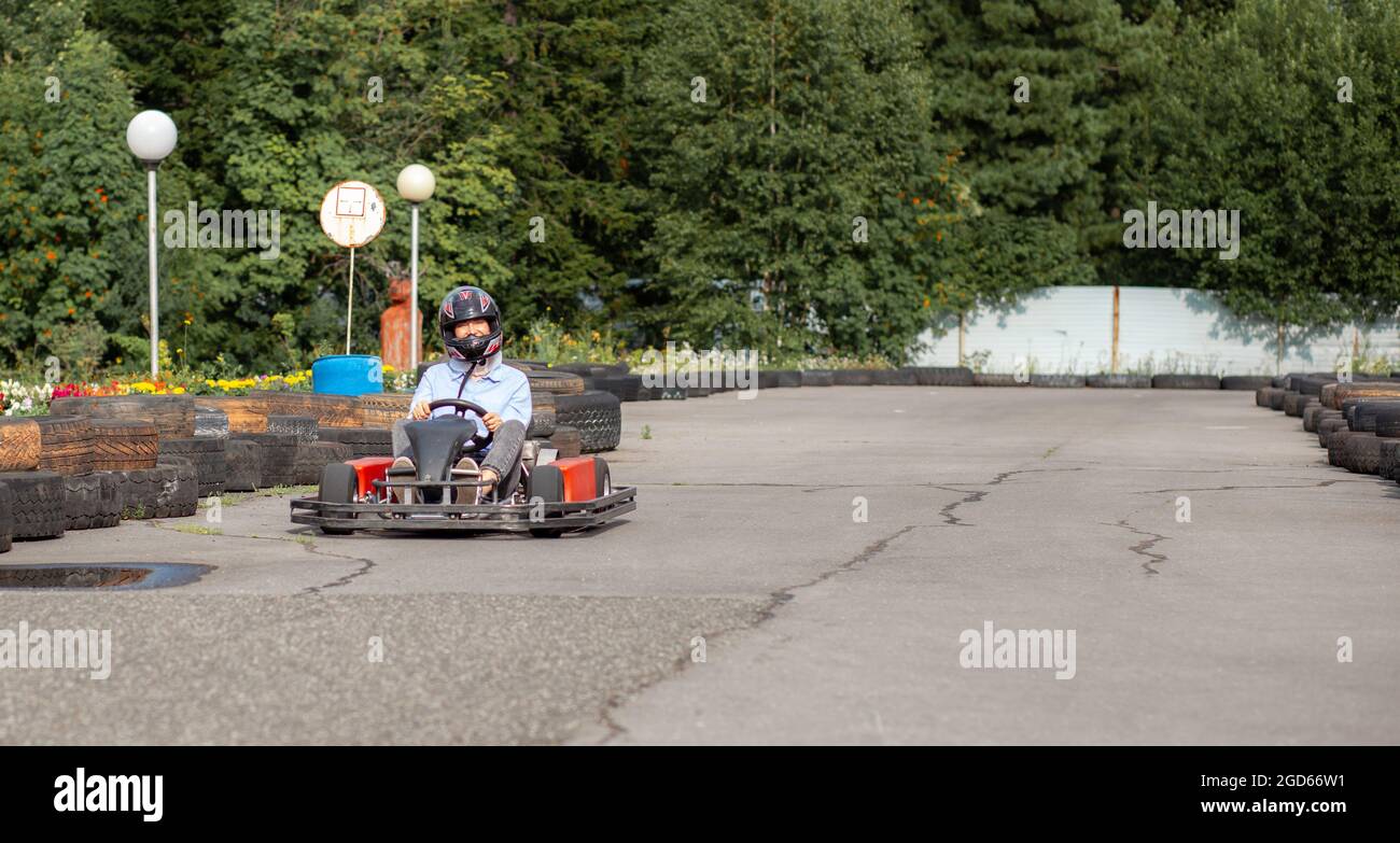 Una ragazza o una donna in un elmetto cavalcano un go-kart su una pista speciale recintata con ruote in gomma. Attività ricreative e sport sui trasporti. Preparazione A. Foto Stock