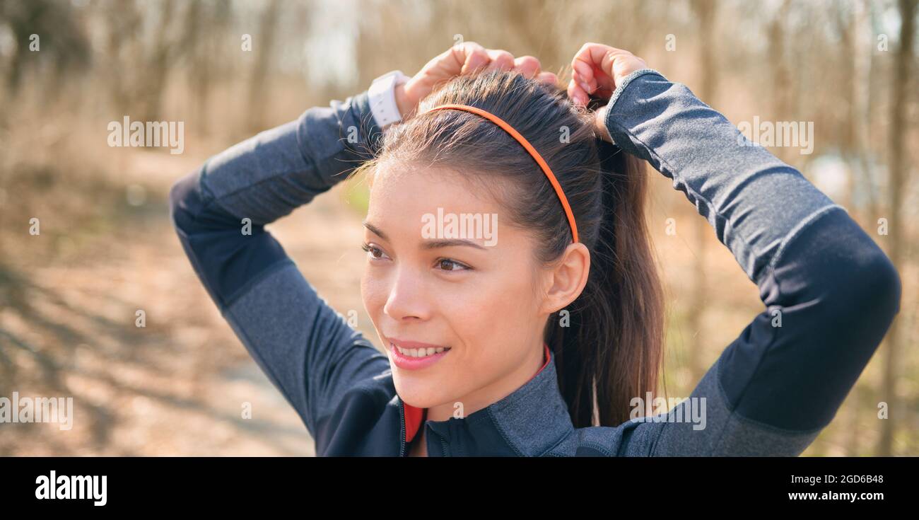 Corridore asiatico sempre pronto a correre fuori legando i suoi capelli in coda di pony per l'allenamento di jogging di hiit. Buon banner jogger dell'atleta sorridente. Foto Stock