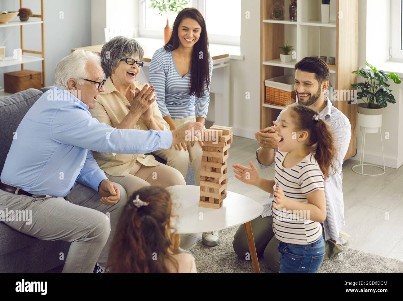 Una famiglia grande felice tutti insieme che gioca il gioco di legno della torre di blocco a casa Foto Stock