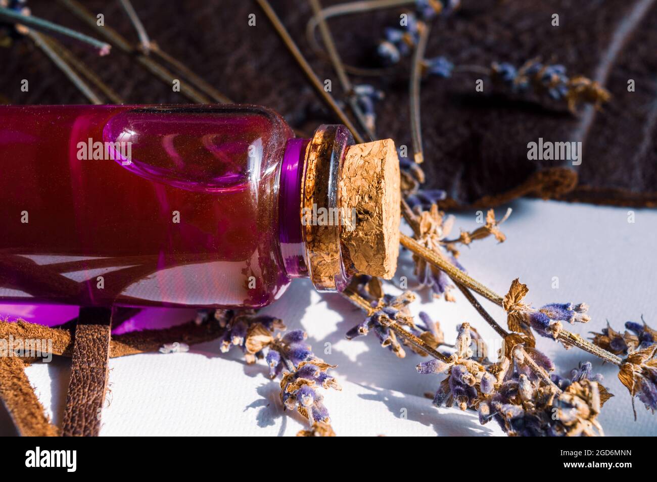 Immagine in primo piano di un flacone con tappo in vetro con liquido rosa e lavanda secca su un notebook aperto. Foto Stock