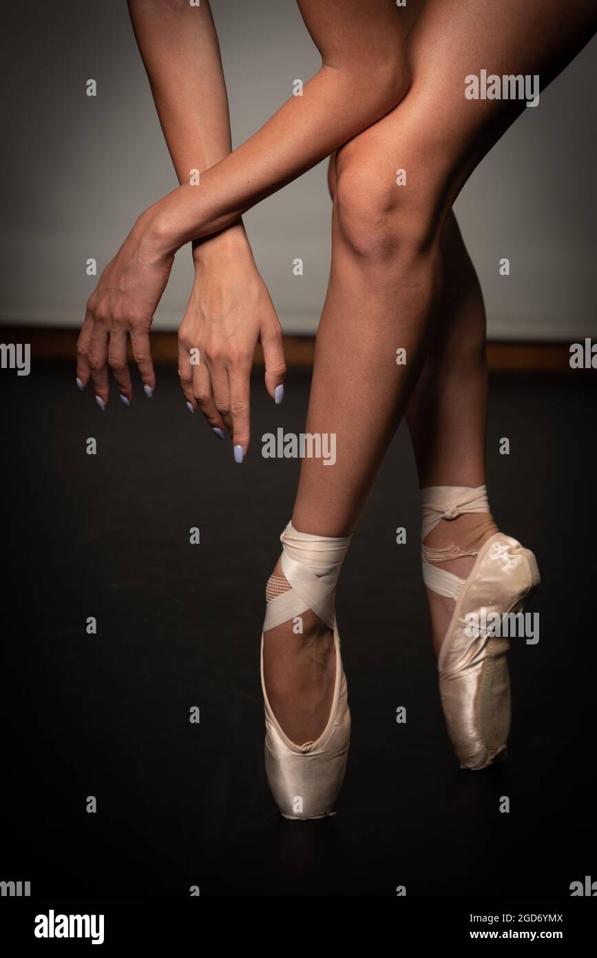 Gambe di ballerina giovane con scarpe da punta che ballano su uno sfondo a pavimento nero. Pratica di balletto. Piedi di ballerina. Foto Stock