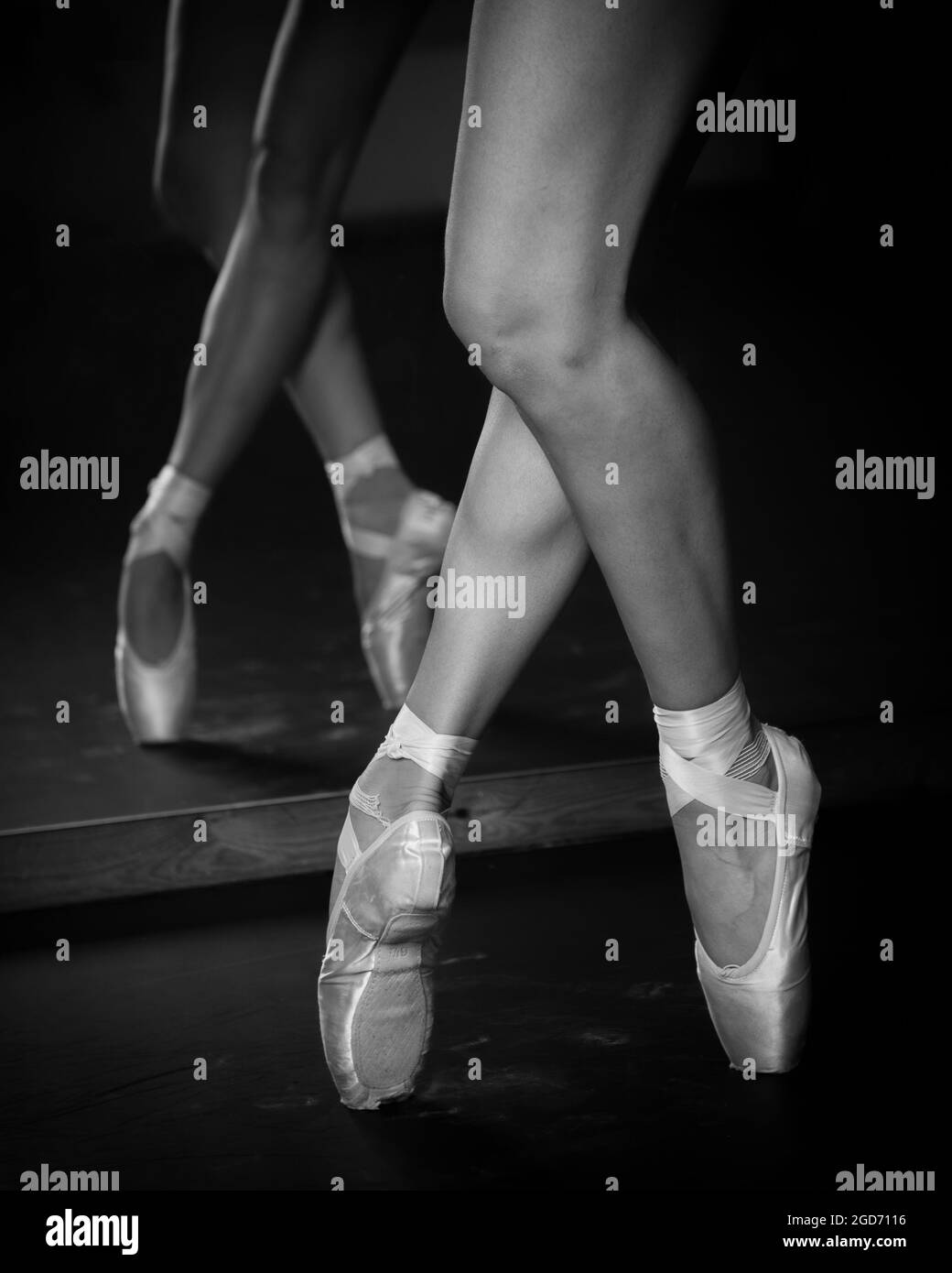 Gambe di ballerina giovane con scarpe da punta che ballano su uno sfondo a pavimento nero. Pratica di balletto. Foto Stock