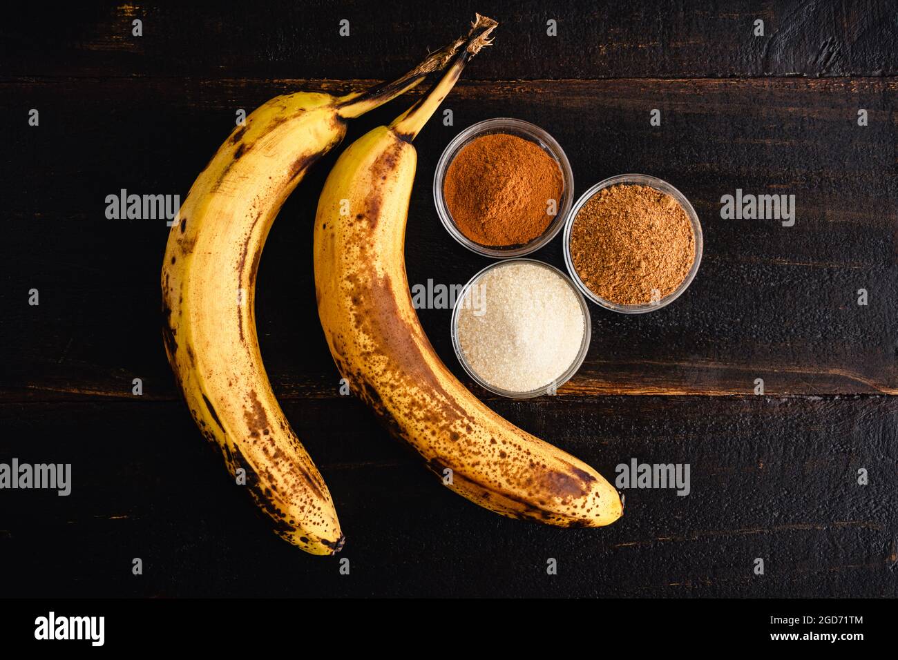Padella banane fritte alla cannella ingredienti su un tavolo di legno: Banane supermature, cannella, zucchero e noce moscata su uno sfondo di legno scuro Foto Stock