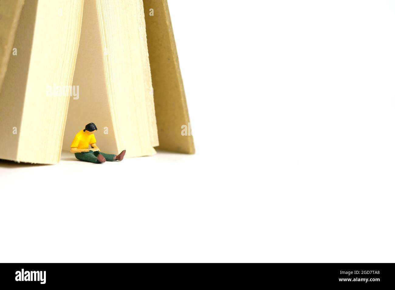 Foto di personaggi giocattolo in miniatura. Uno studente di uomini seduto sotto la tenda del libro, isolato su sfondo bianco. Foto immagine Foto Stock